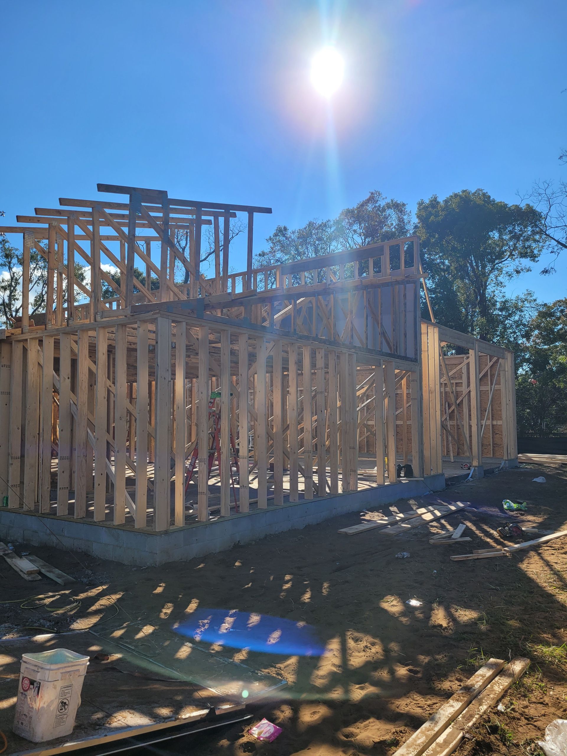 A house is being built on a sunny day with the sun shining through the trees.