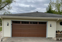A white house with a brown garage door and a black roof.