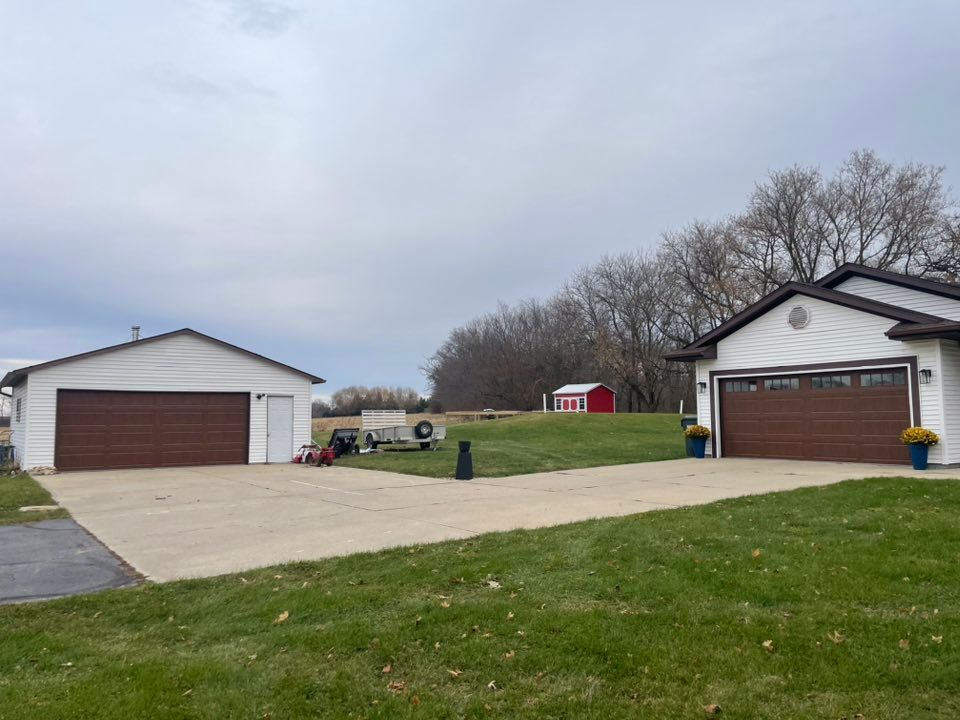 Two garages with brown doors and a grassy lawn under a cloudy sky.