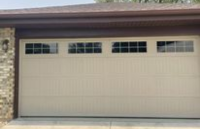 There is a long, almond-colored garage door with square window clusters near top of door.