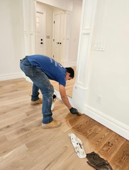 Person applying finish to hardwood floor in a home.