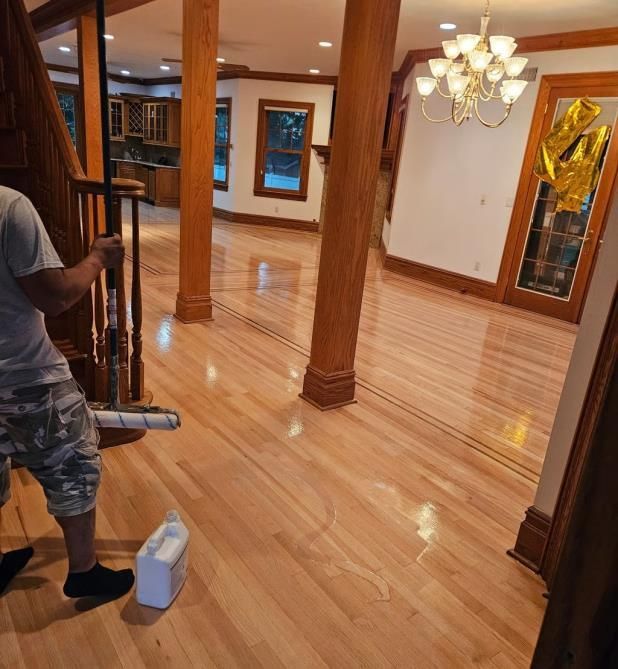 Person cleaning hardwood floor with a mop; interior view of a room with natural light and a chandelier.