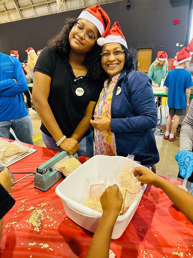A woman and a girl wearing santa hats are standing next to each other at a table.