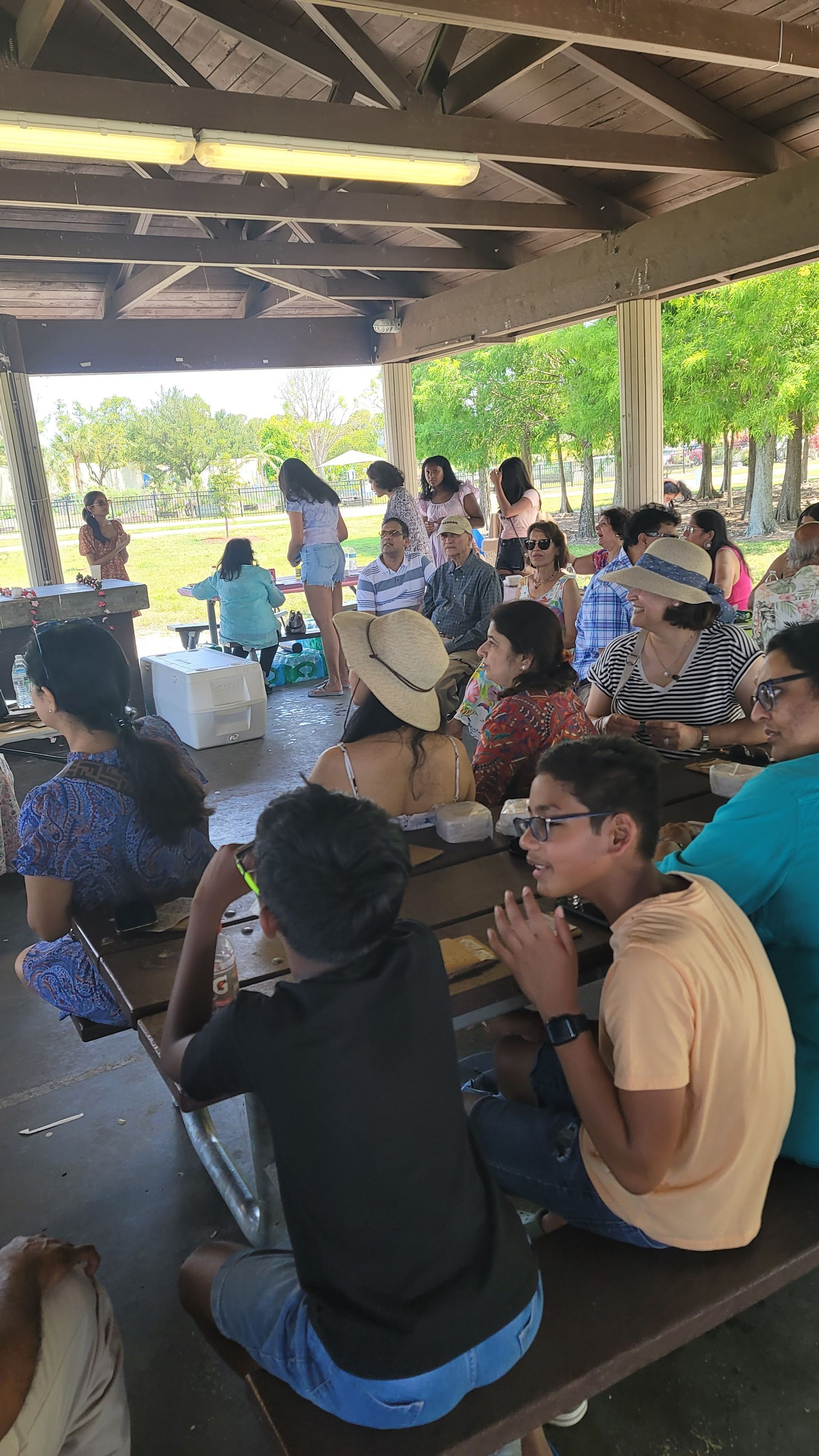 Group of people at a picnic shelter. Some are clapping while others watch someone speaking outside.
