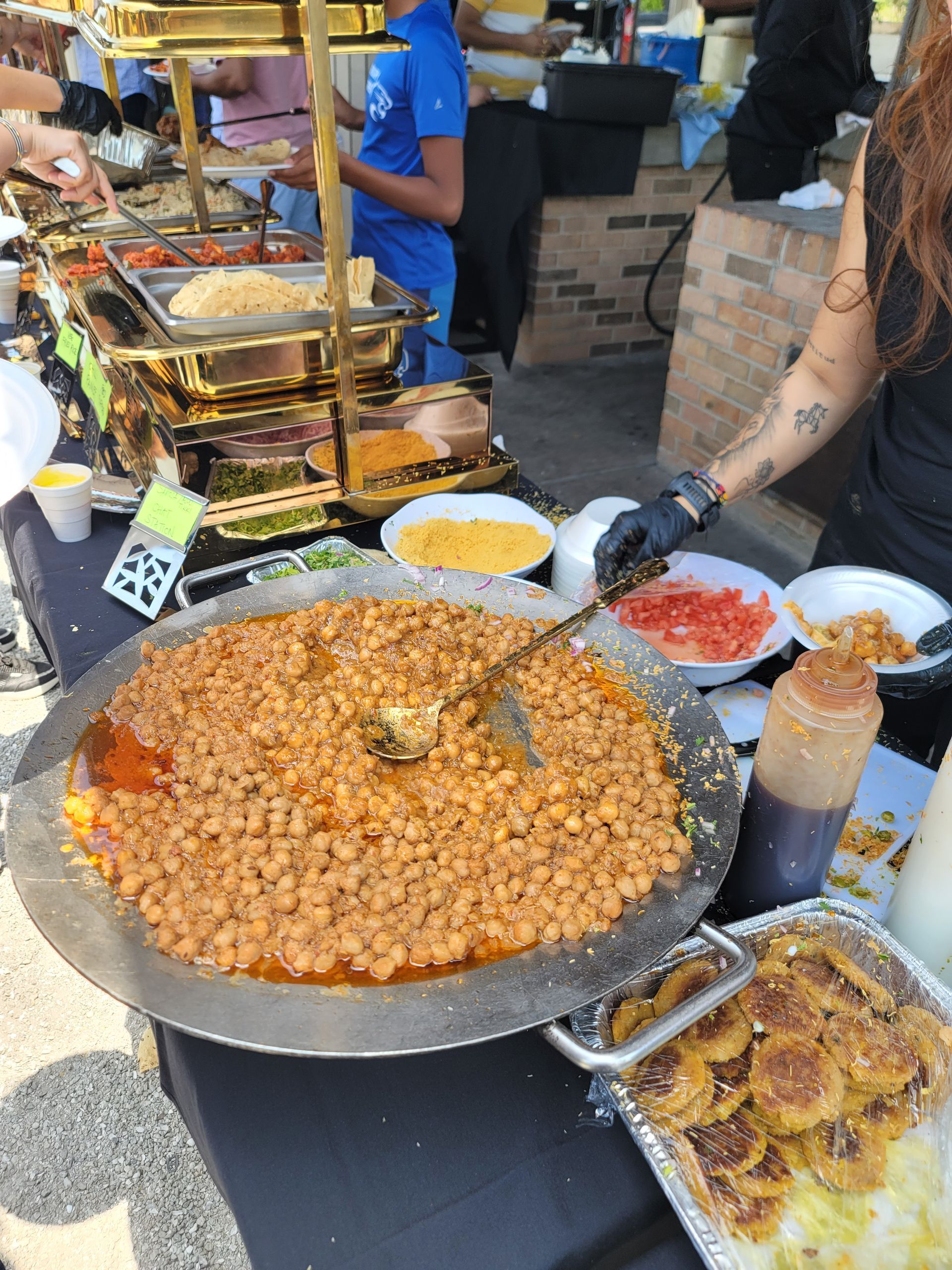 Food stall with large pan of chickpeas, toppings, and servers.