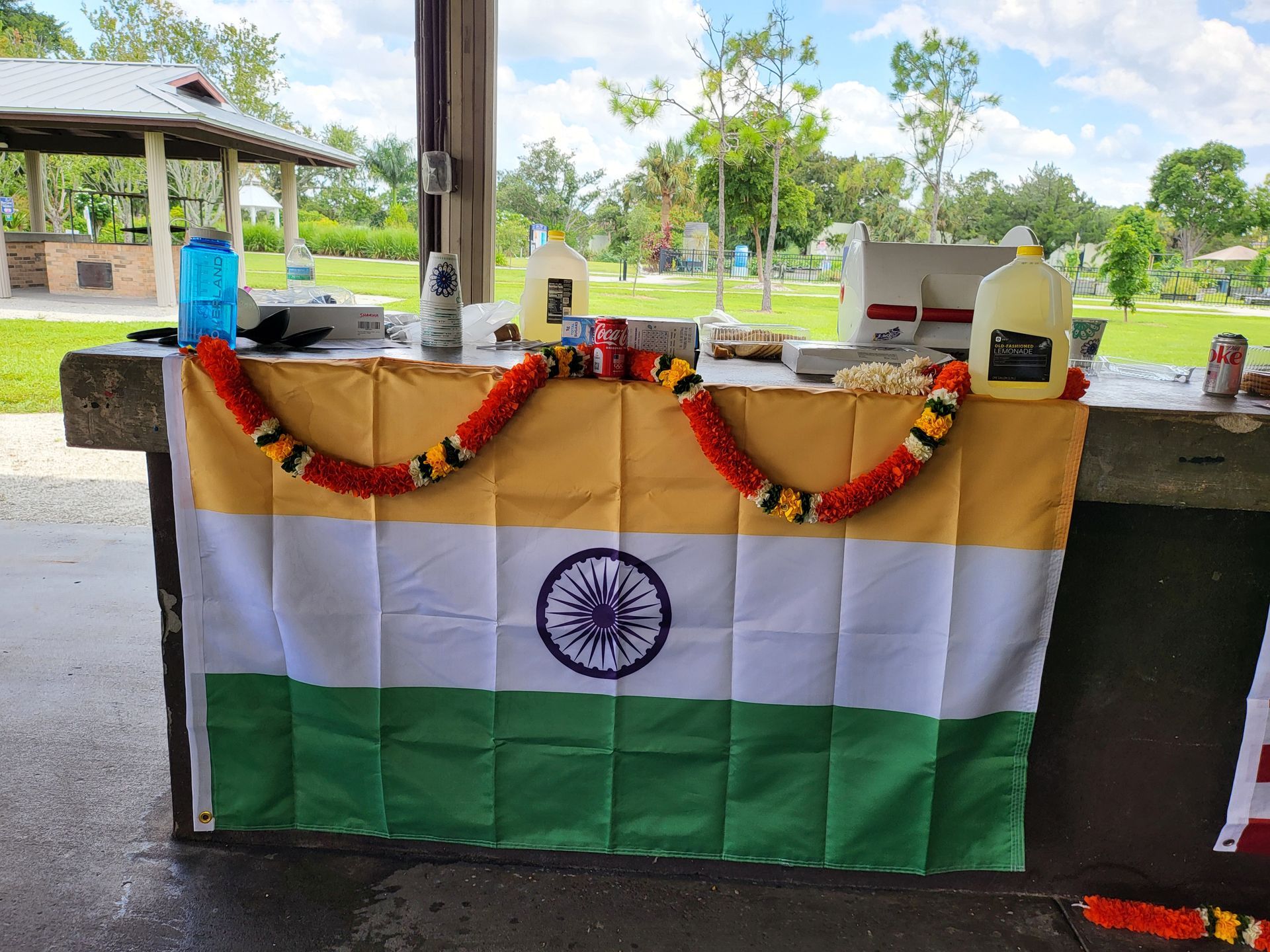 Indian flag draped over a table outdoors; decorated with garland and bottles.