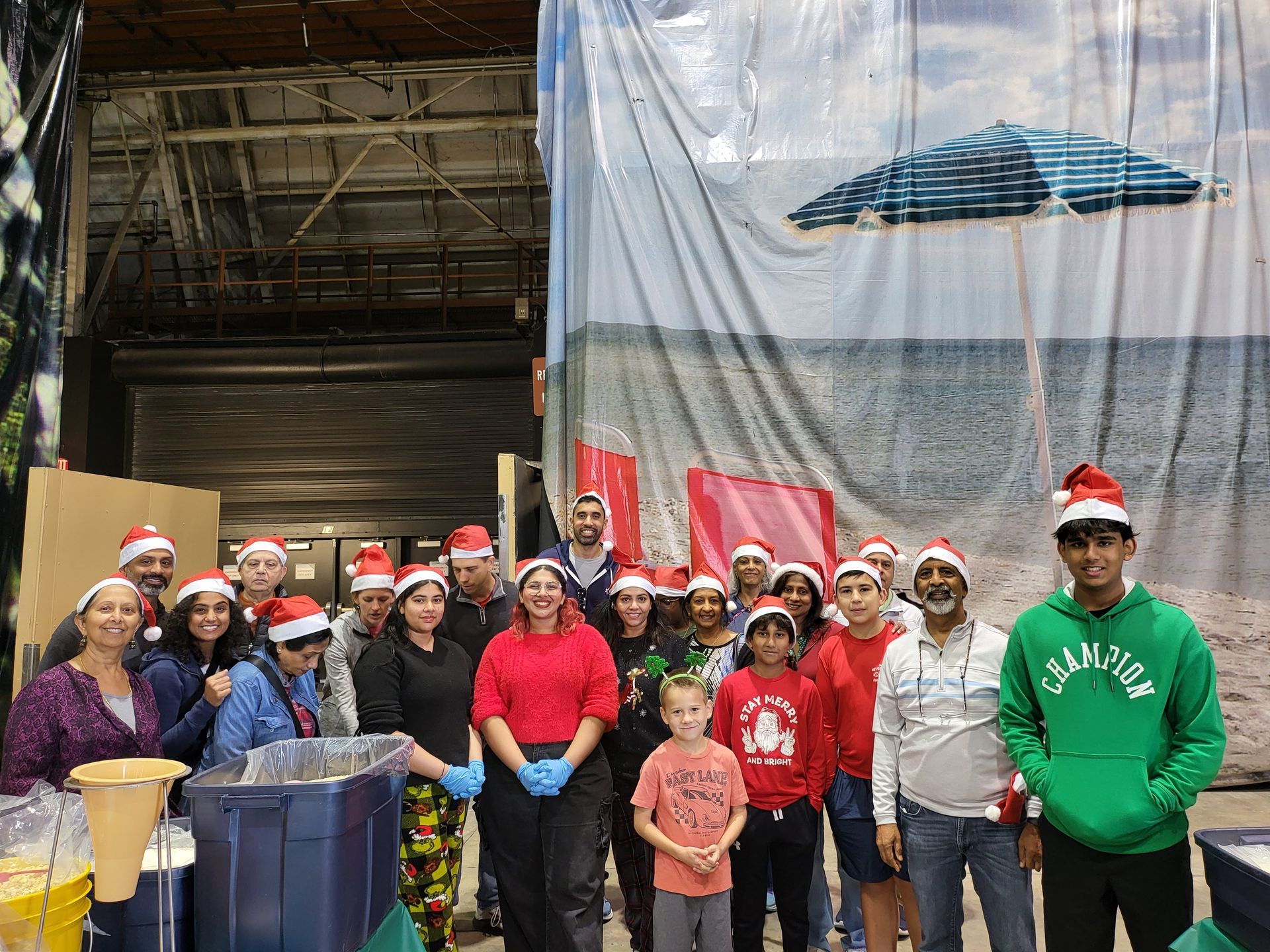 Group of people in Santa hats, smiling in front of a beach scene backdrop.