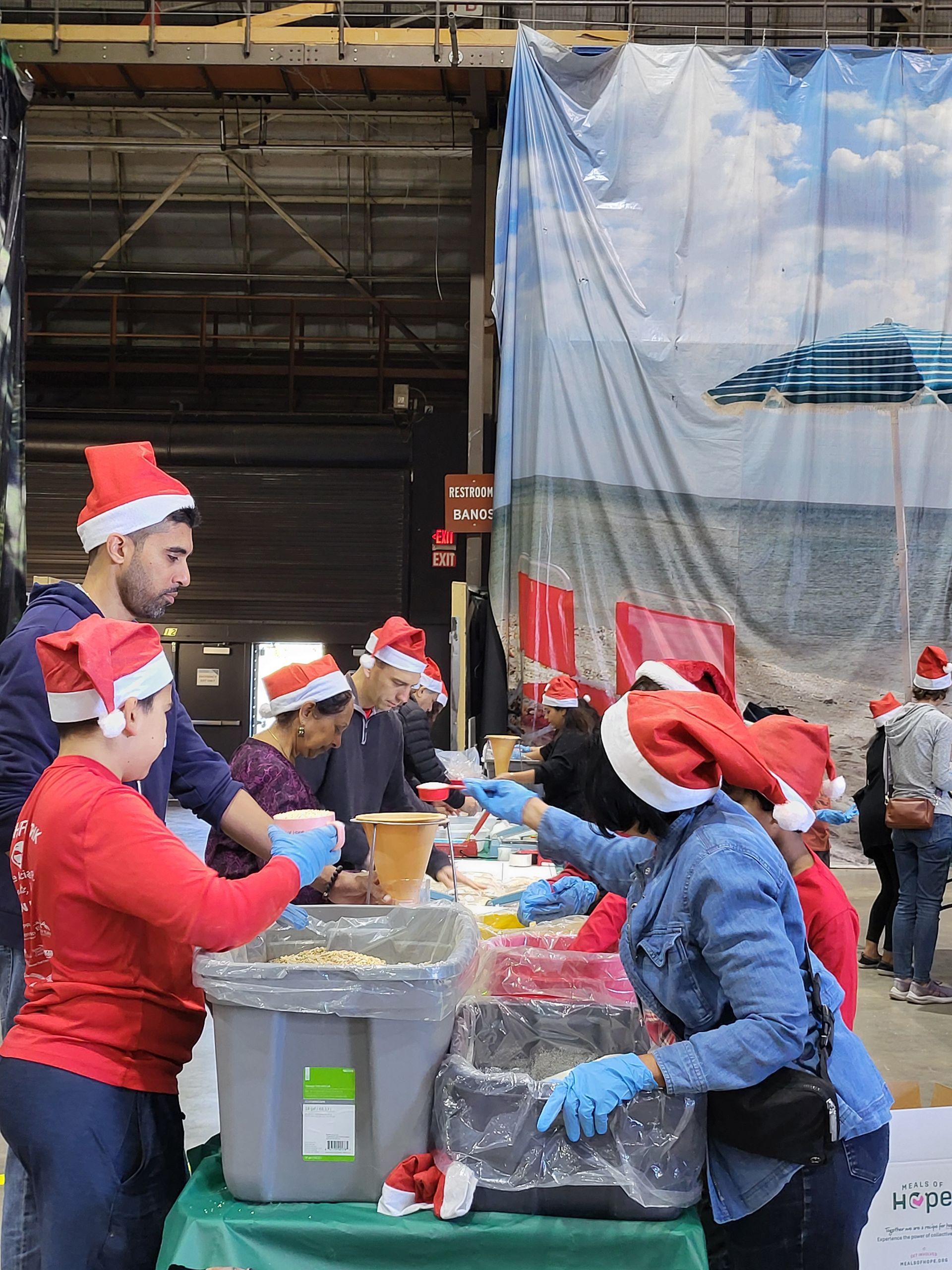 People in Santa hats serve food at an outdoor event.