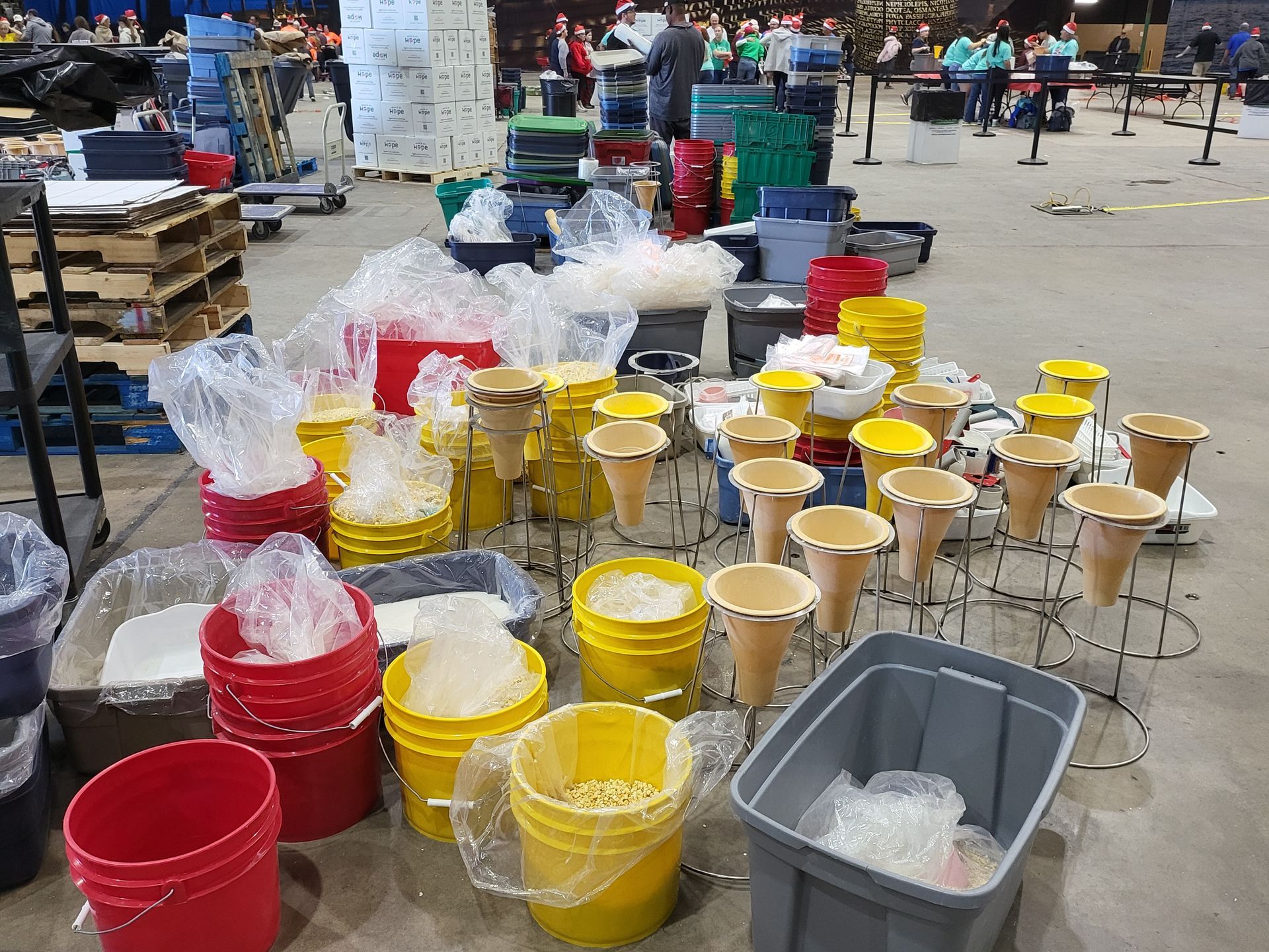 Buckets, cones, and bins with materials set up in a large warehouse. People in background.