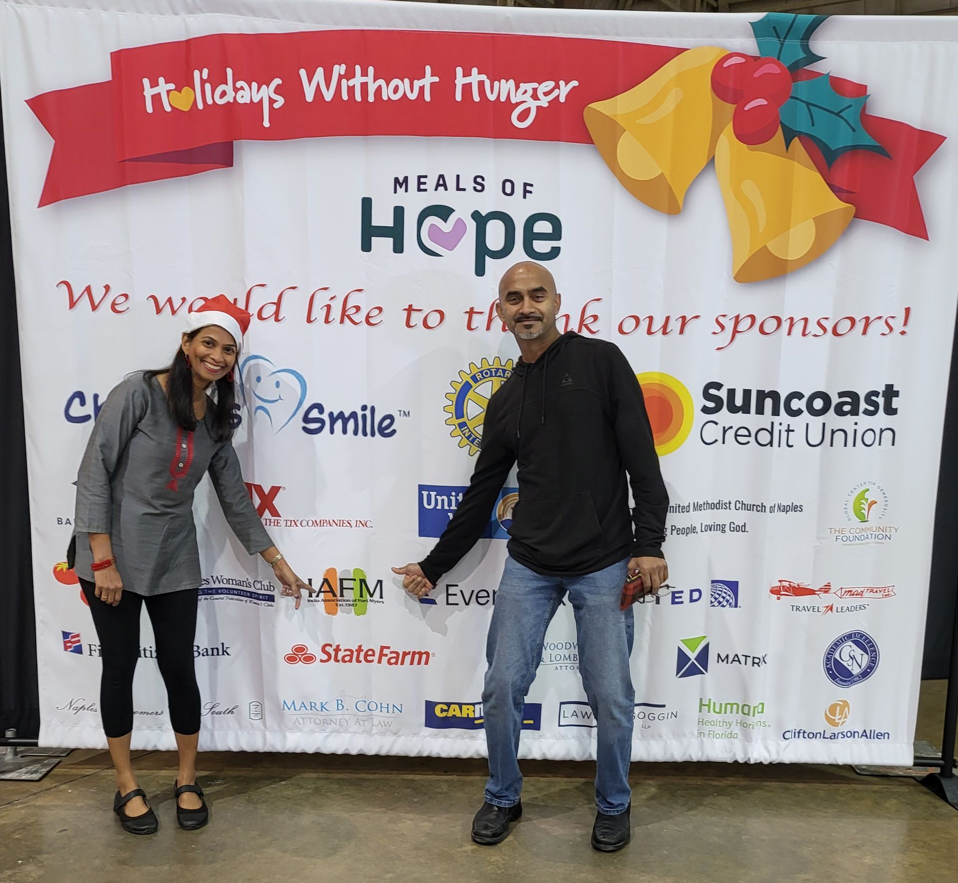 Two people pose in front of a sponsor banner for 