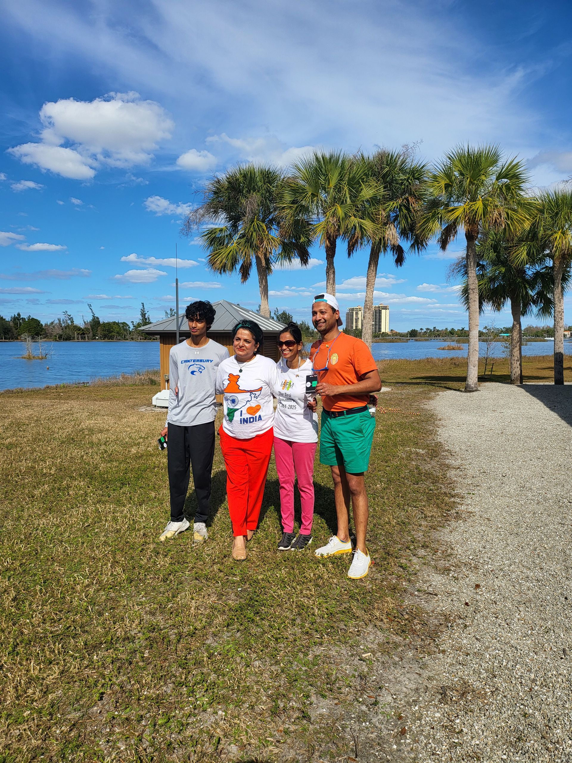 Family of four poses outdoors near water under a bright blue sky.