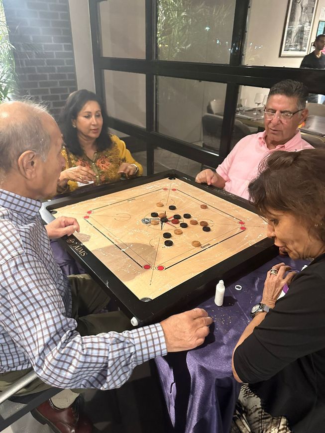 A group of people are sitting around a table playing a game of carrom.