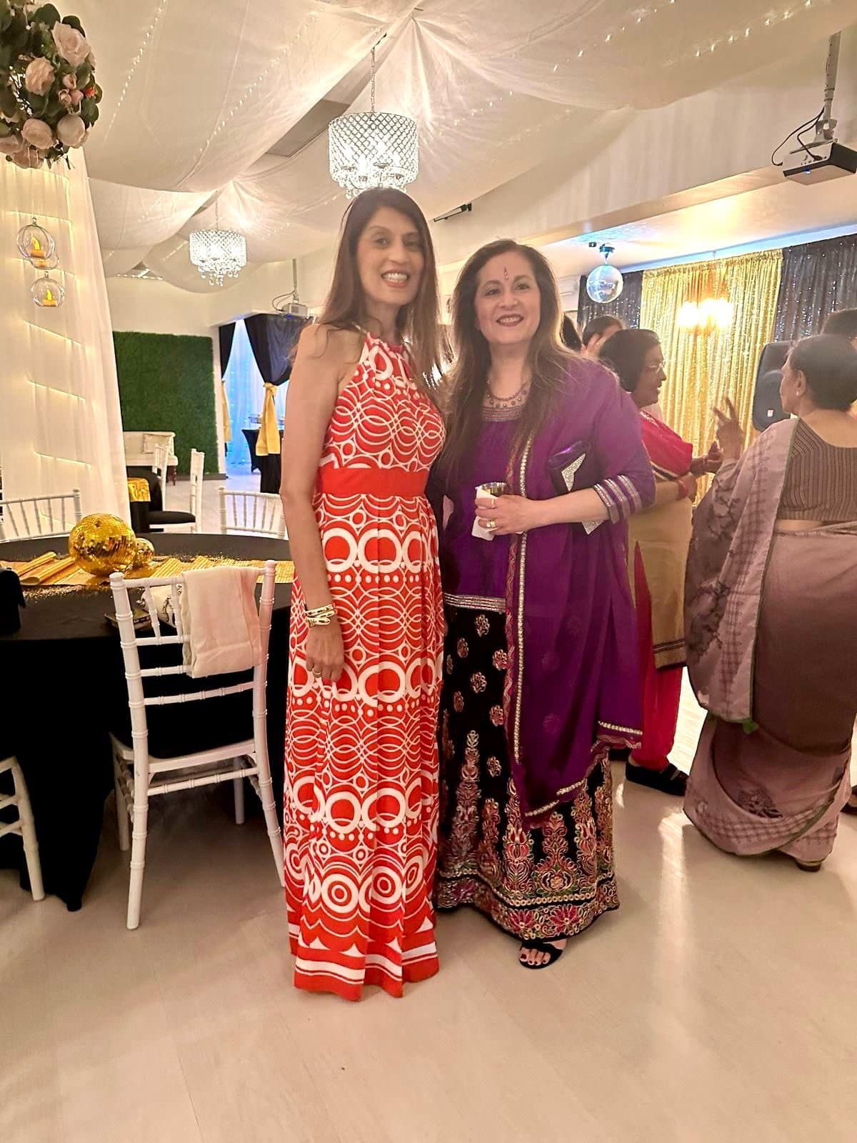Two women are standing next to each other in a room at a party.