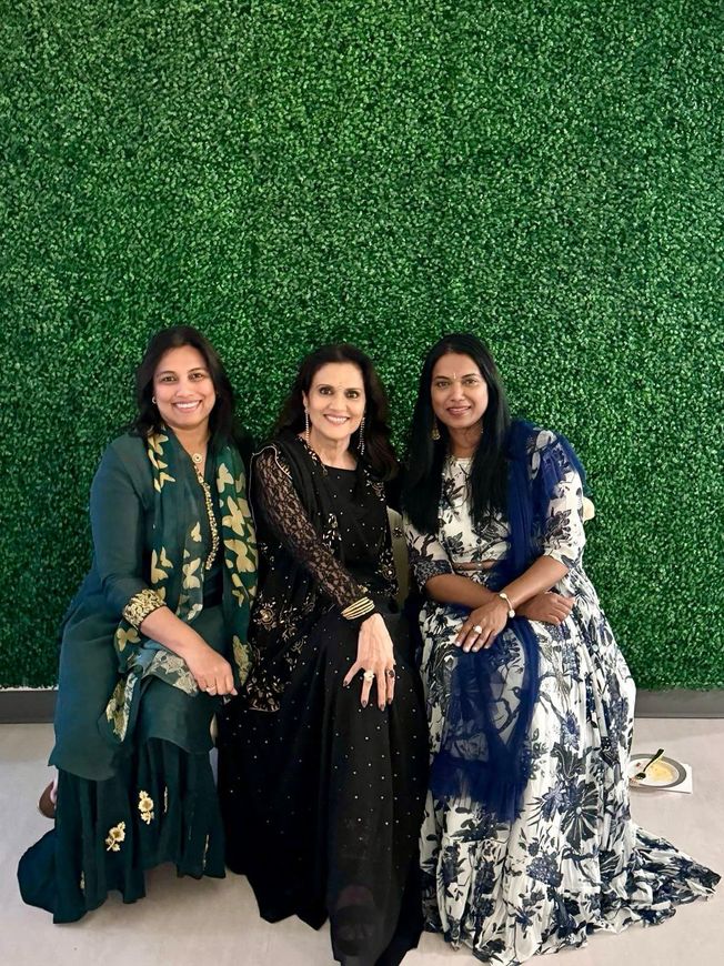 Three women are posing for a picture in front of a green wall.