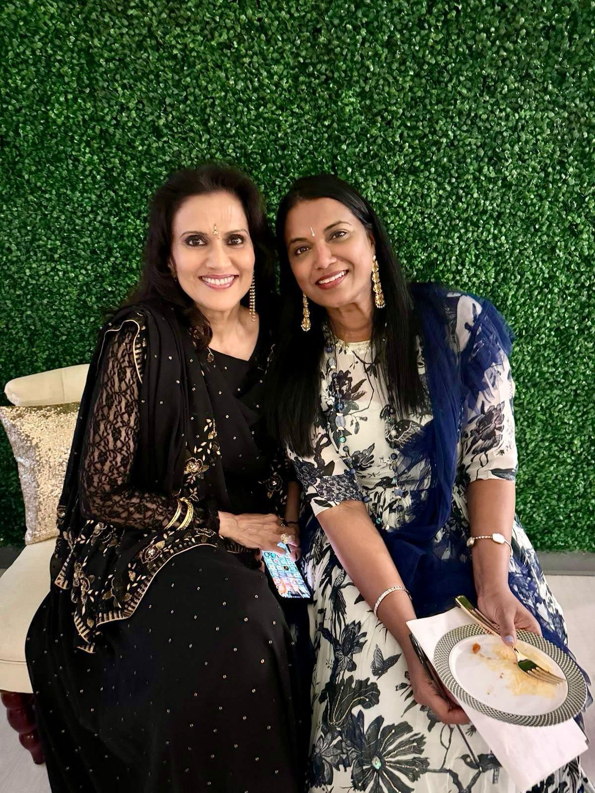 Two women are sitting next to each other in front of a green wall.