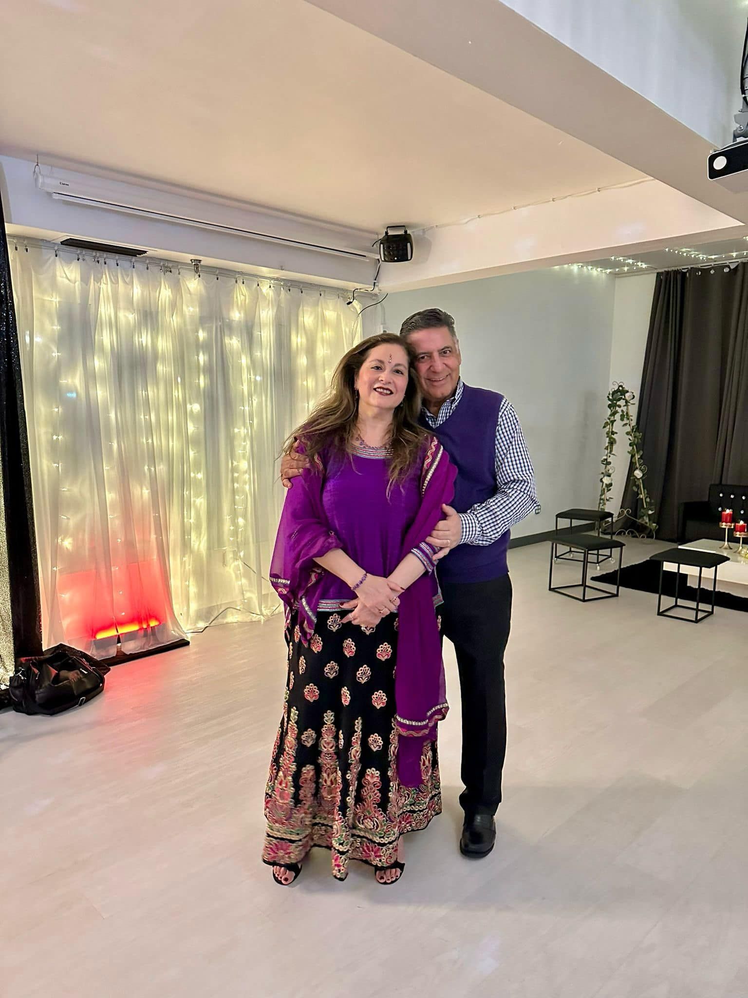 A man and a woman are posing for a picture in a room . the woman is wearing a purple dress.