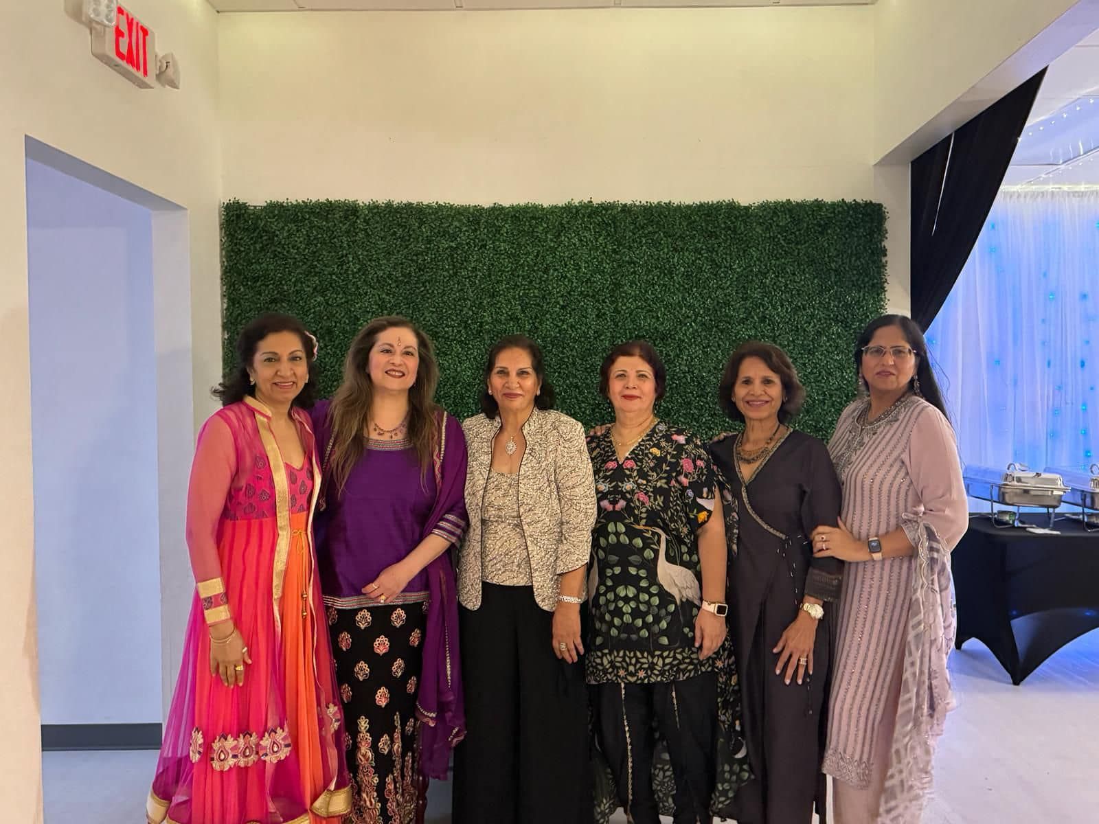 A group of women are posing for a picture in front of a green wall.