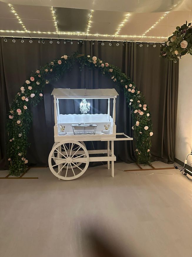 A white cart is sitting in front of a floral arch in a room.