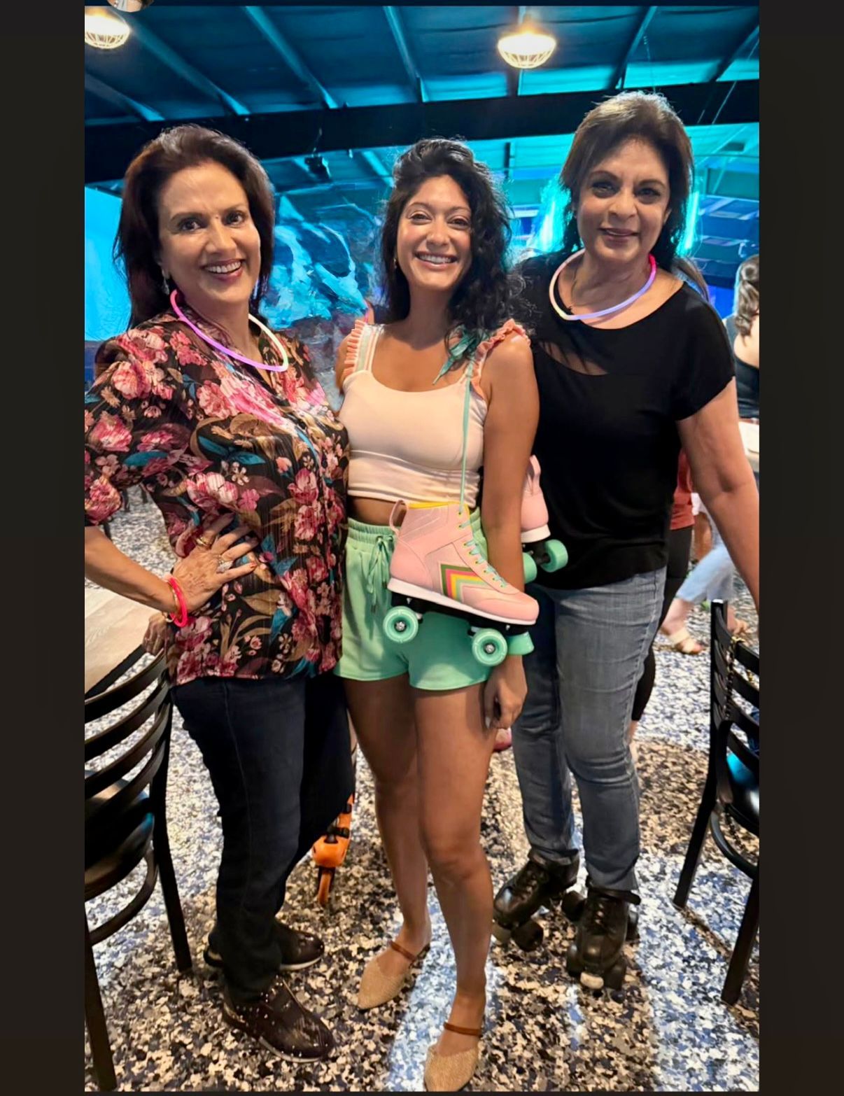 Three women in a restaurant; center woman in shorts and roller skates, flanked by women, one with floral shirt and one with black top.