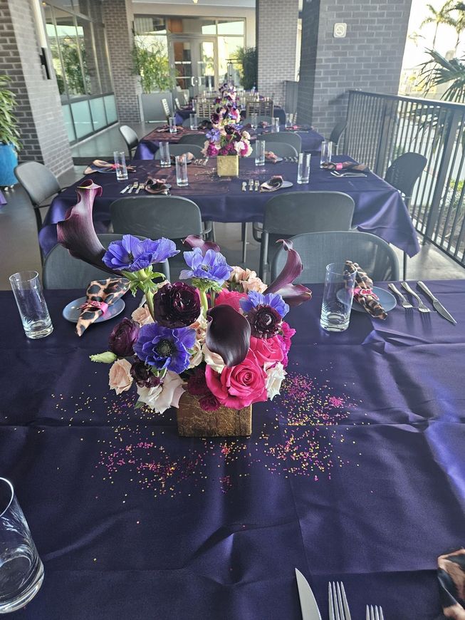A table with a purple tablecloth and a vase of flowers on it.