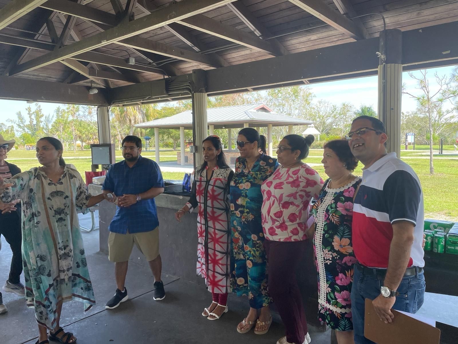 Group of people gathered outdoors under a pavilion, some are speaking and smiling.
