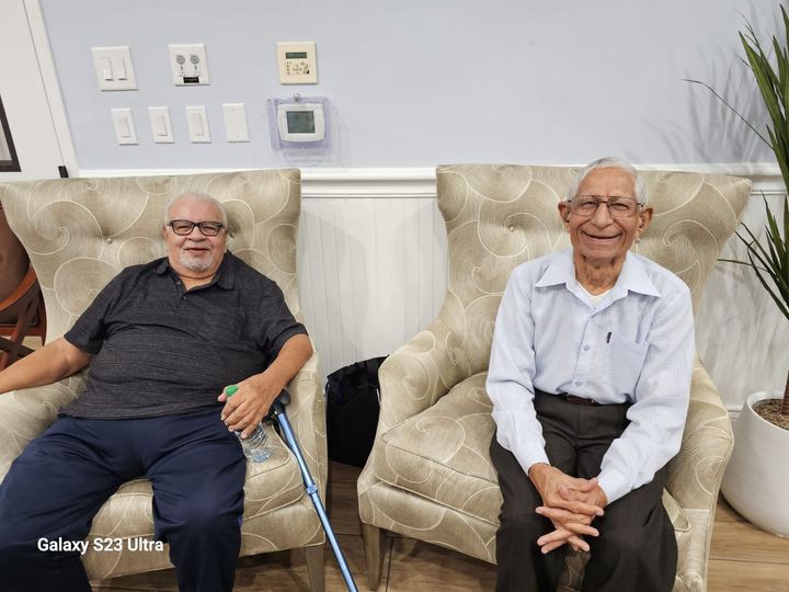 Two older men are sitting in chairs in a living room.