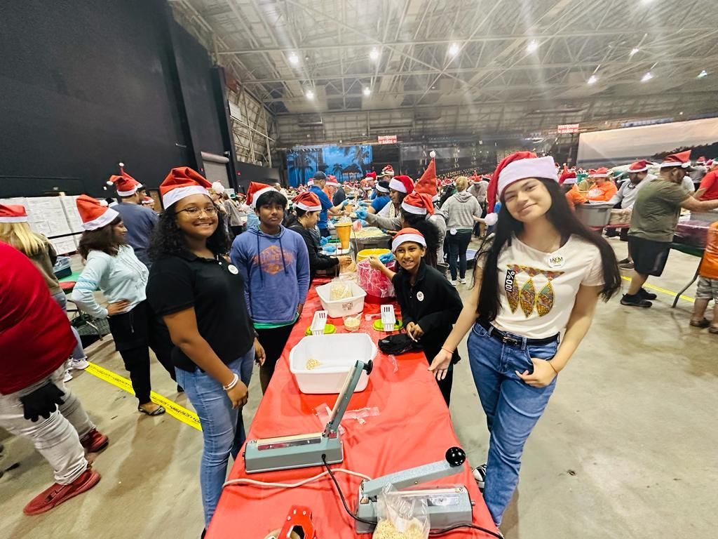 A group of people wearing santa hats are standing around a table.