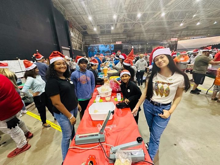 A group of people wearing santa hats are standing around a table.