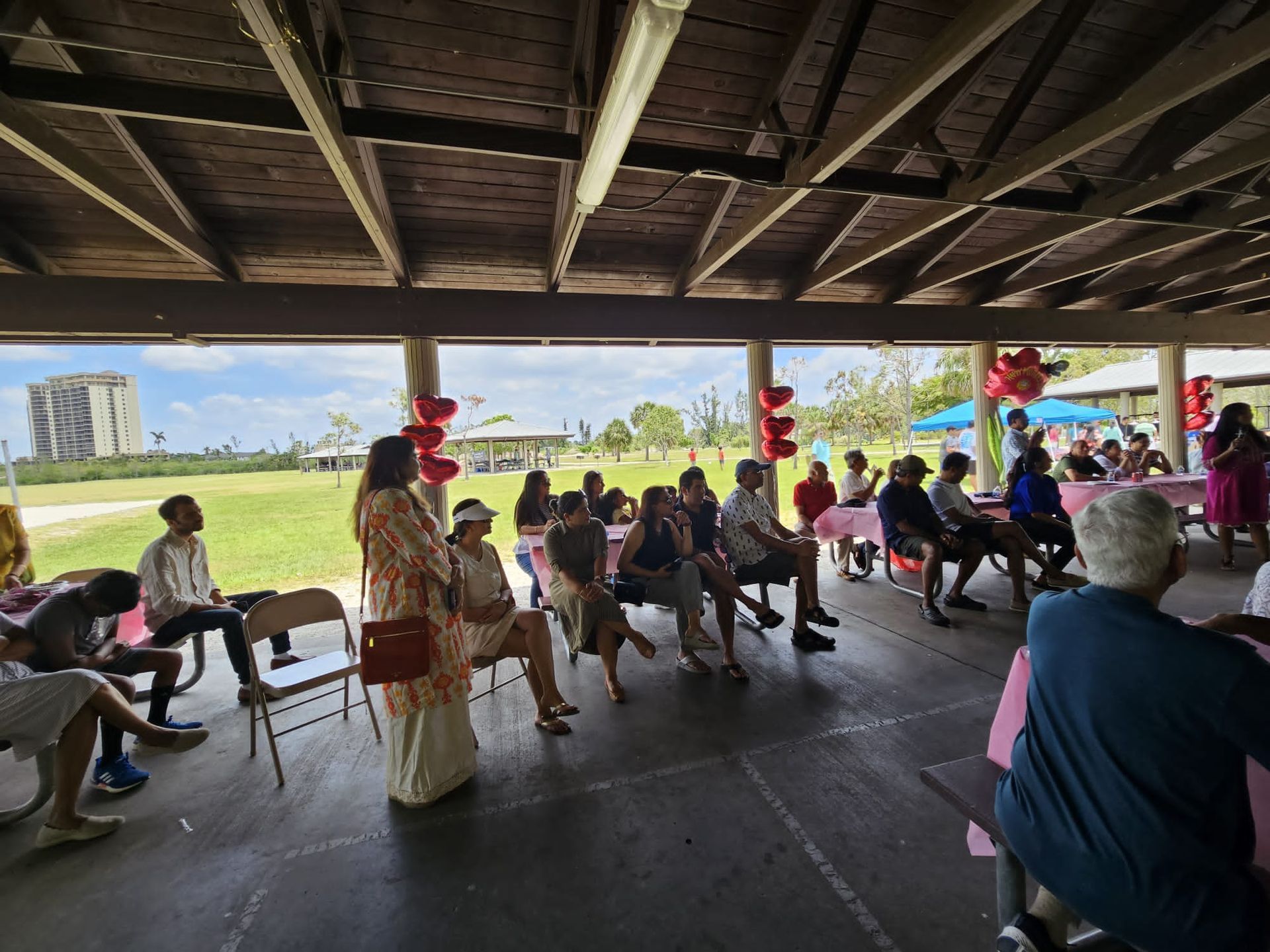 A group of people are sitting under a pavilion in a park.