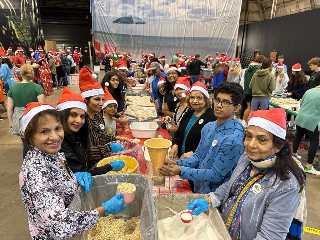 A group of people wearing santa hats are standing around a table.
