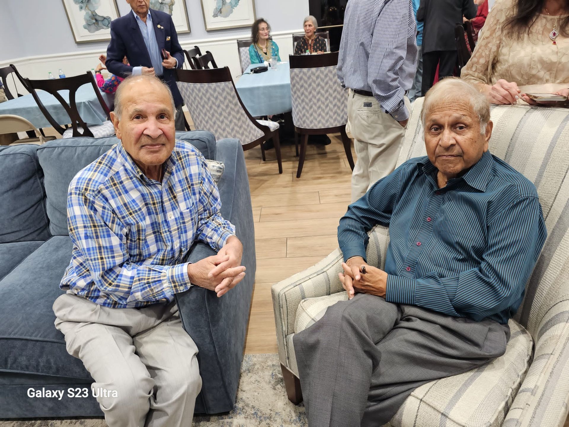 Two older men are sitting in chairs in a living room.