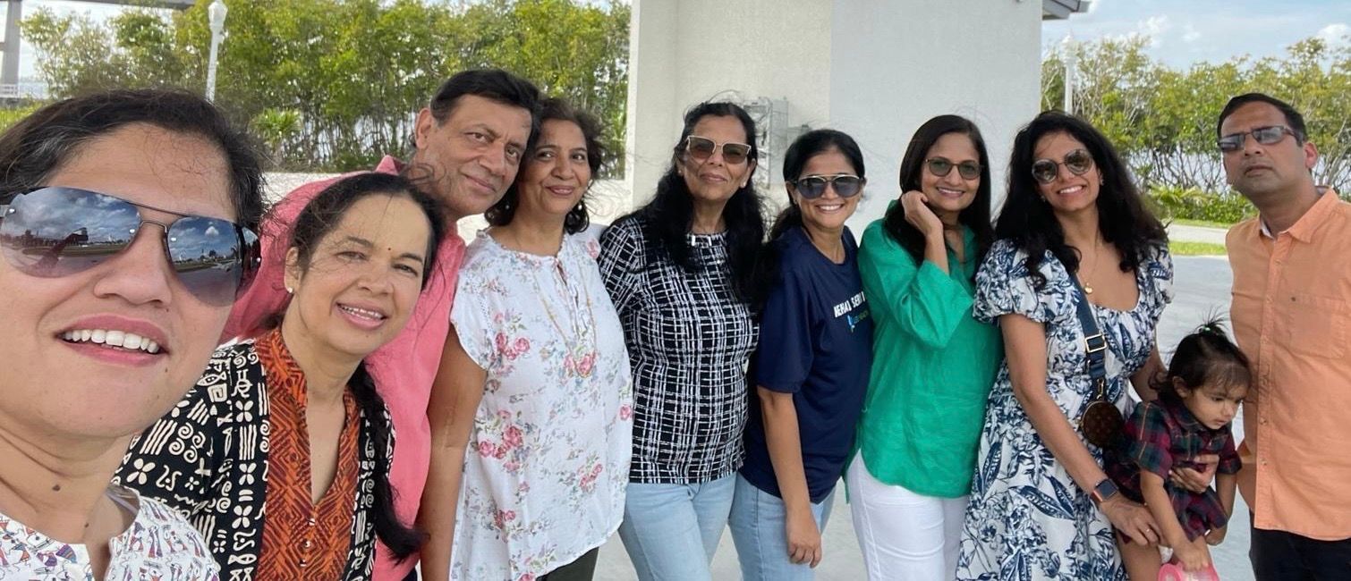 A group of people smiling, posing for a photo outdoors near foliage.
