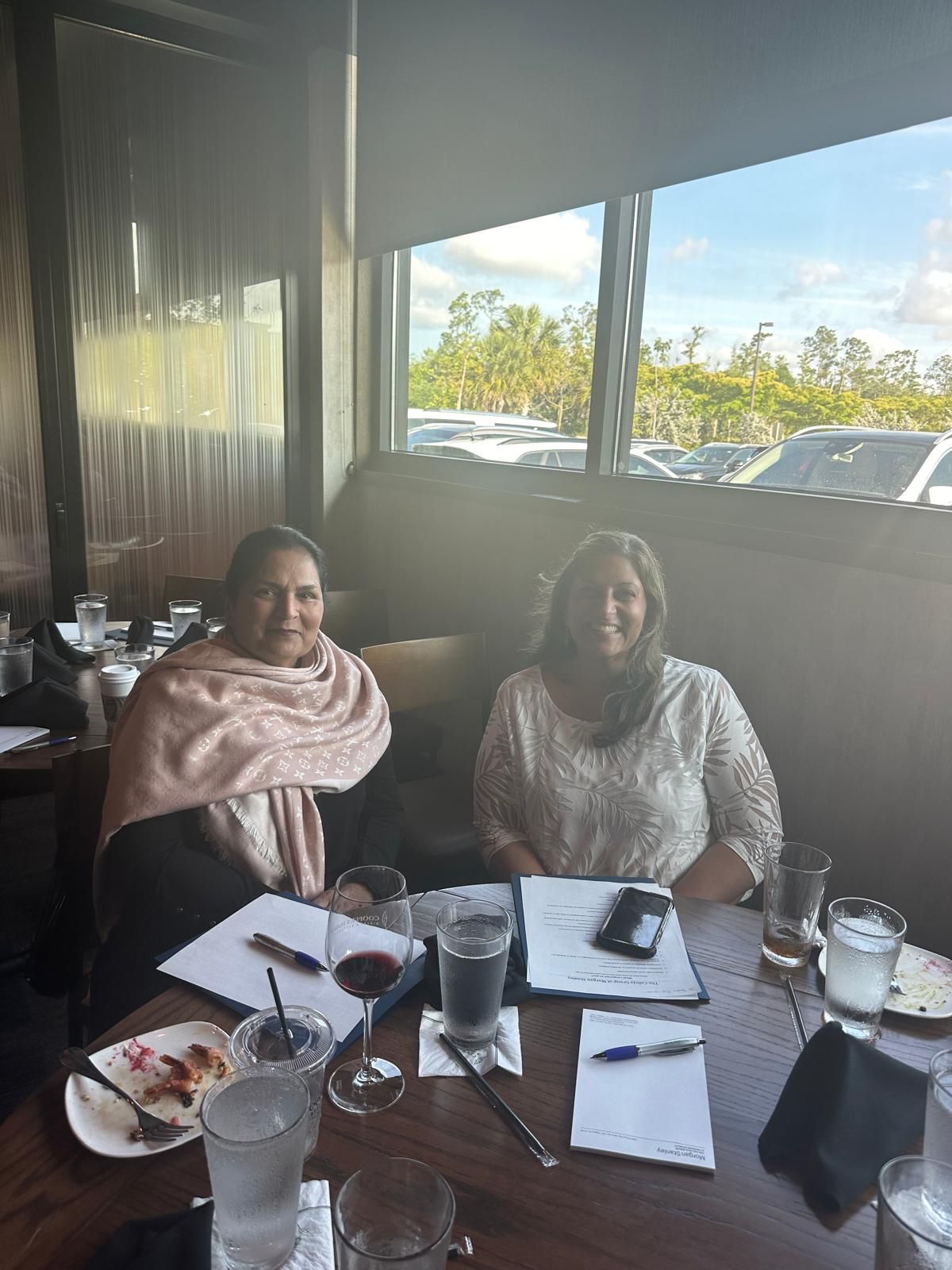 Two women seated at a table in a restaurant, papers and drinks are visible.