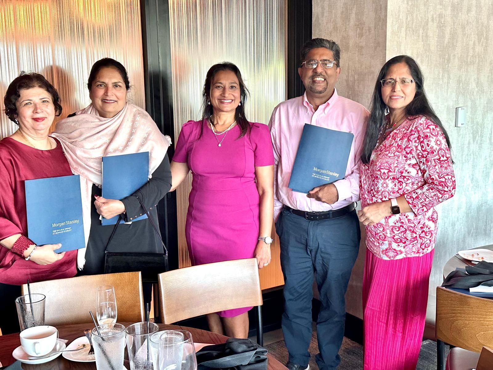 Five people smiling, holding blue folders, in a restaurant setting.