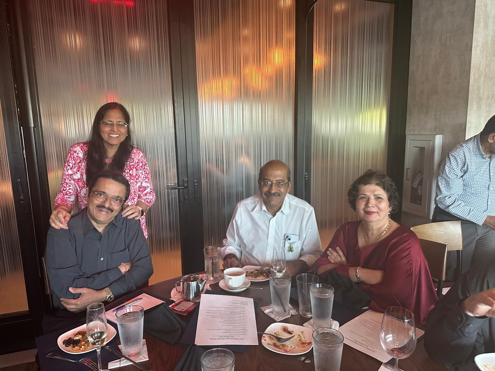 Group of people seated at a table in a restaurant, smiling, with drinks and food, enjoying a meal.