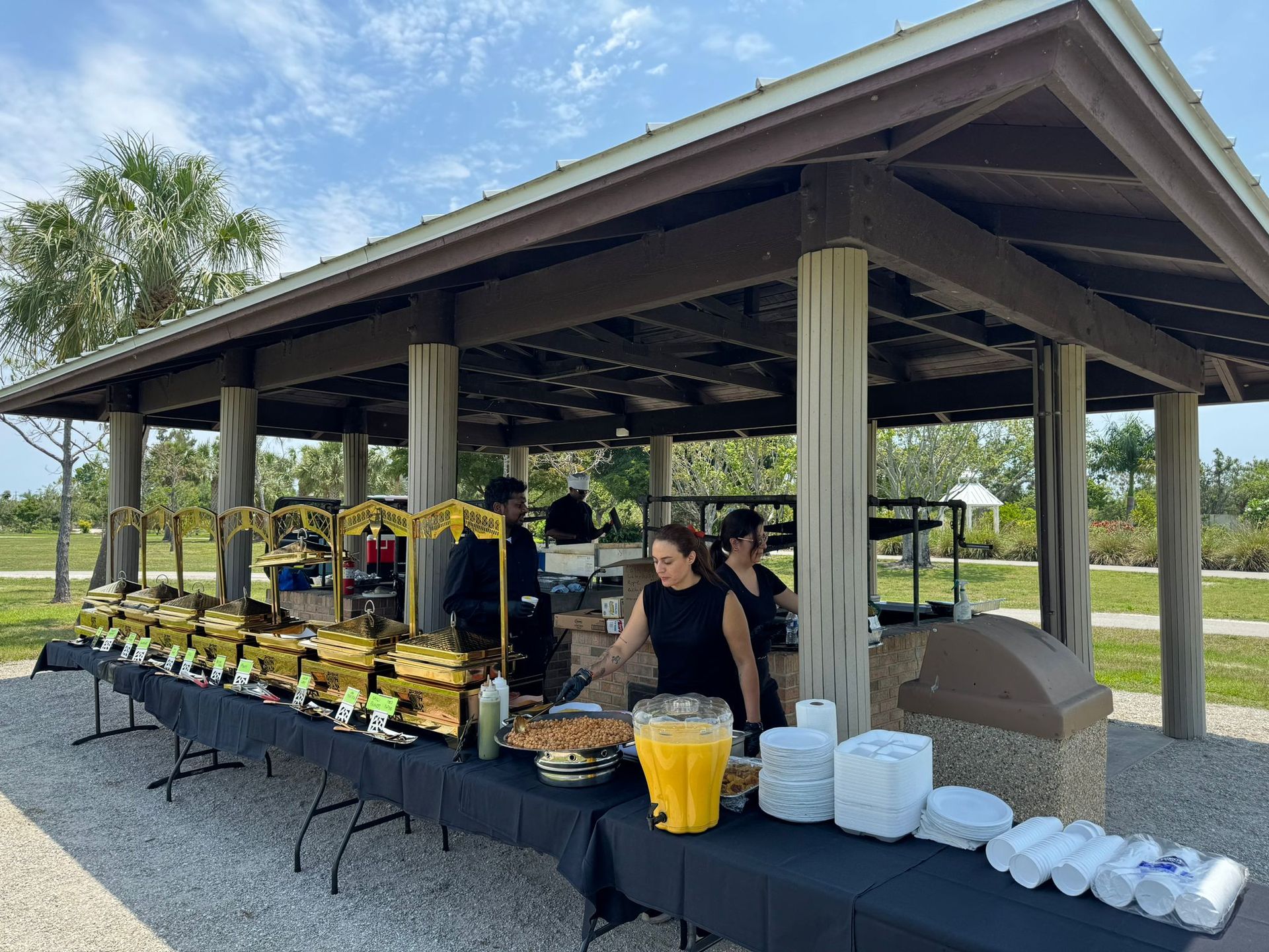 Buffet setup under a pavilion; staff serving food outdoors; various dishes displayed.