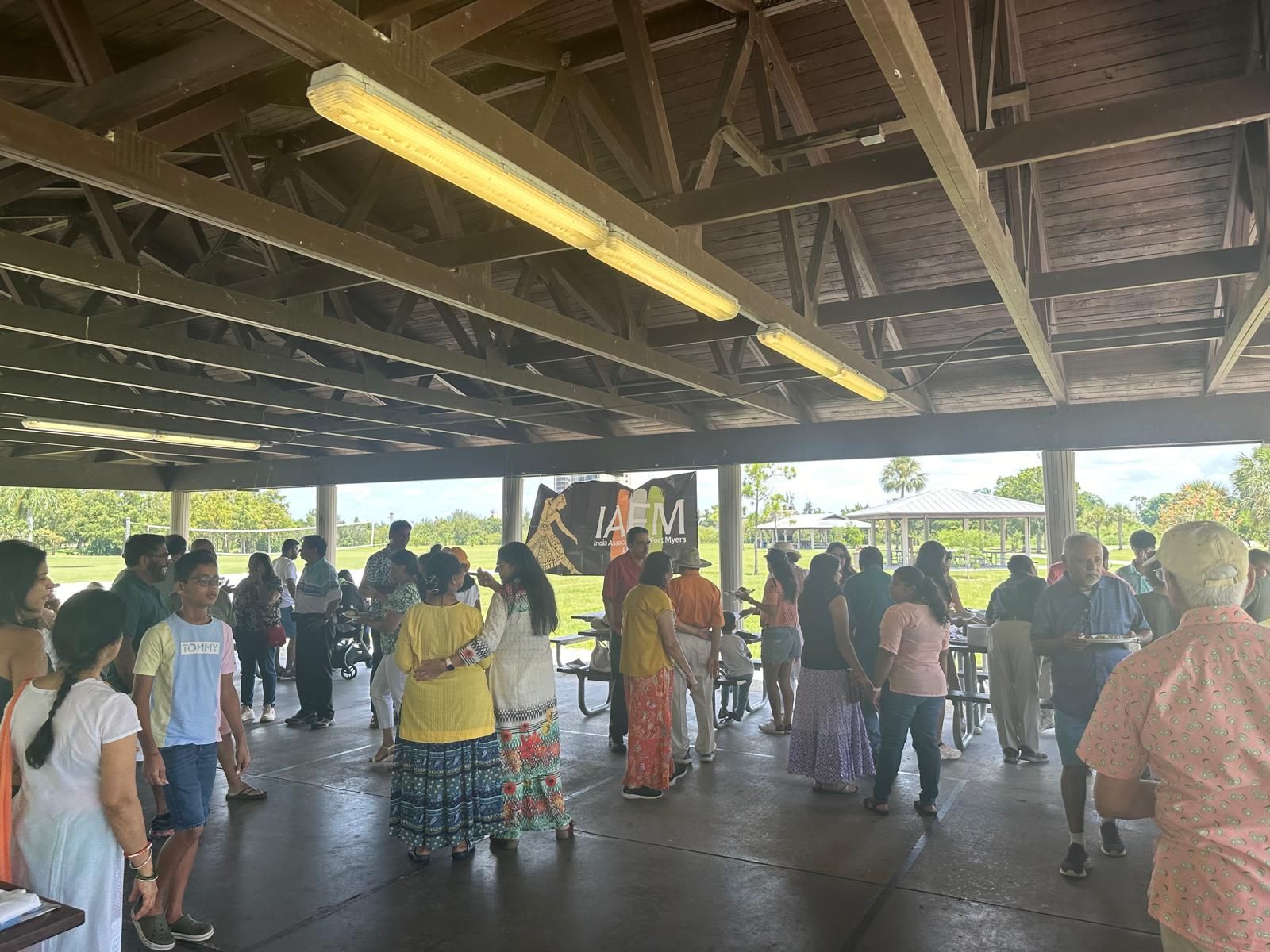 People gathered under a pavilion. Some are talking, others standing. The roof is wood.