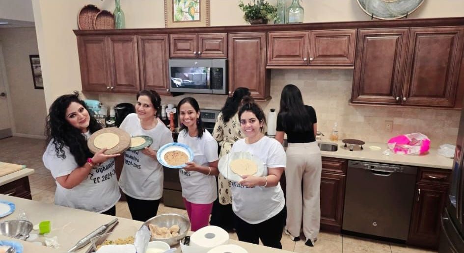 Group of women in a kitchen holding up food plates. They are smiling and gathered around the counter.