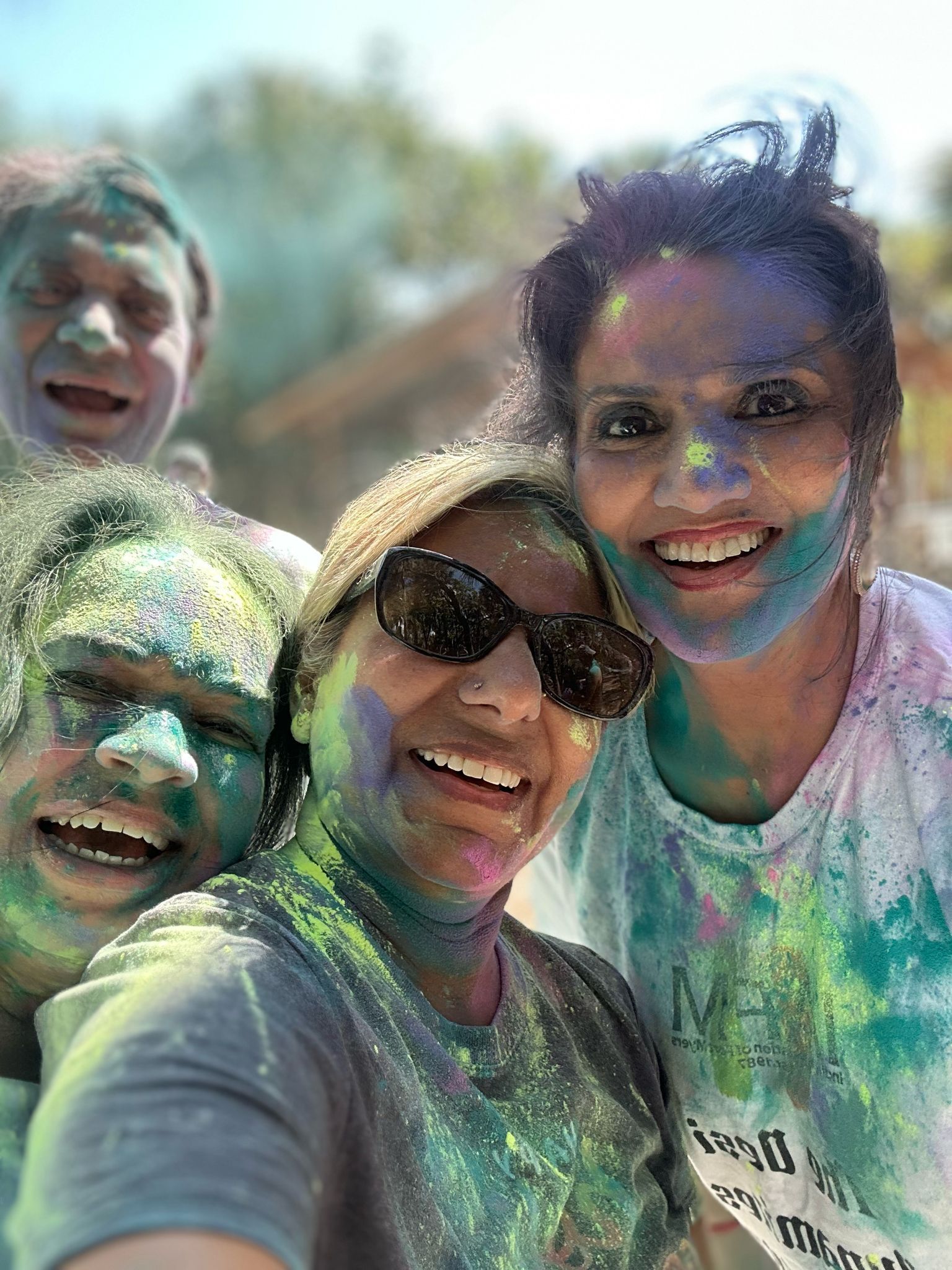 People smiling, covered in colorful powder, celebrating Holi festival.