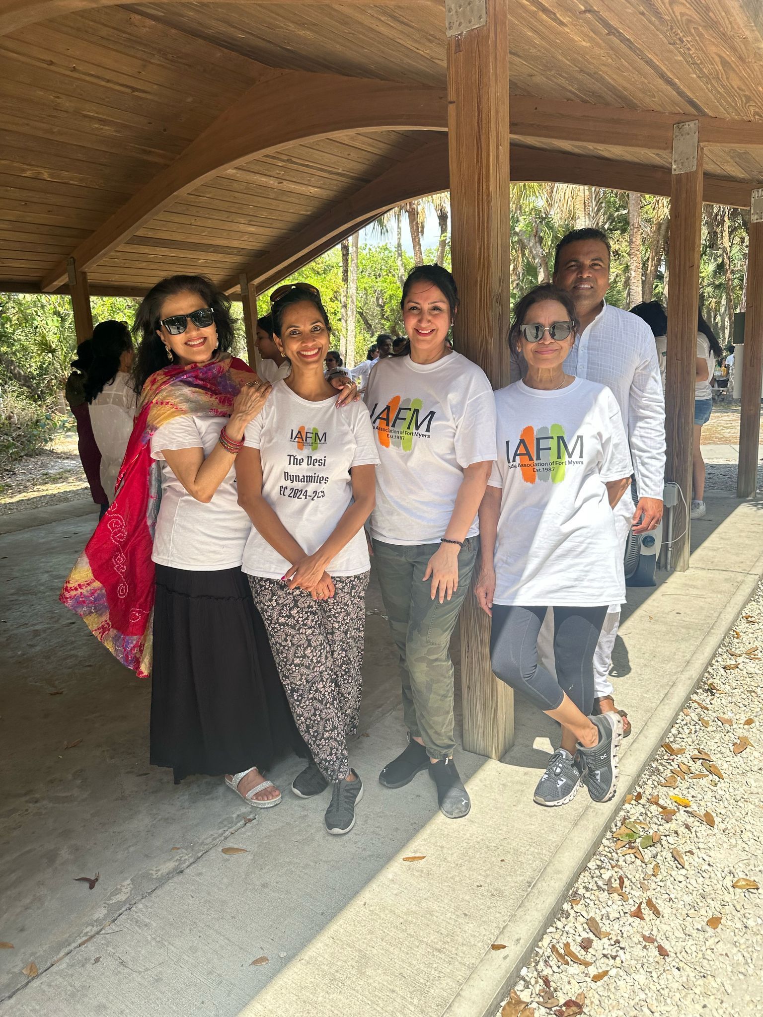 Group of five people smiling outdoors under a wooden structure.