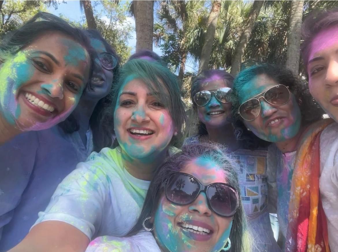 Group of women with colorful powder on faces; celebrating outdoors, smiling.