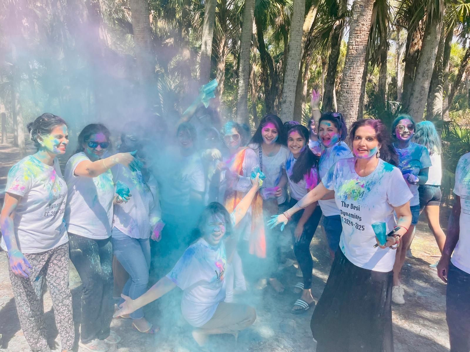 Group of people celebrating with colorful powder, outdoor setting, smiles.