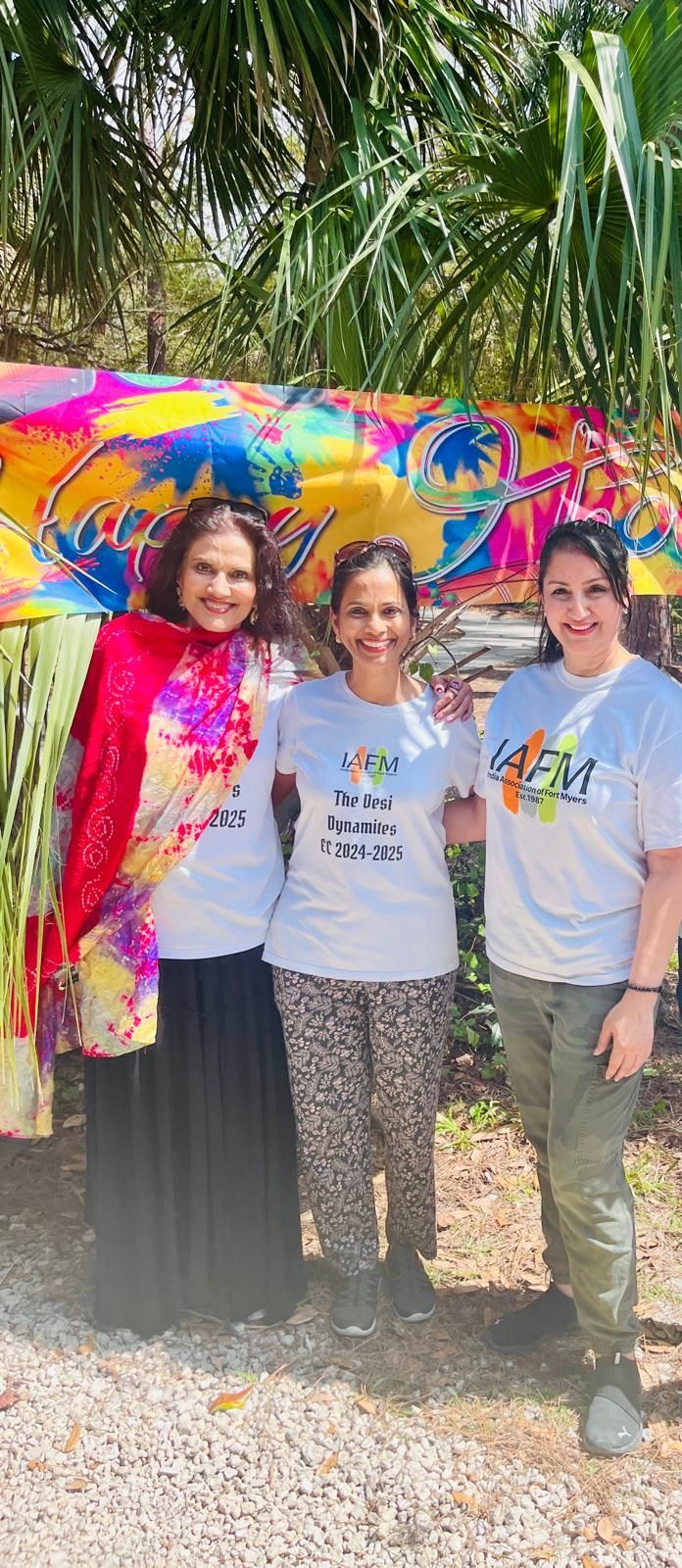 Three women smiling, posing outside in front of colorful decorations.