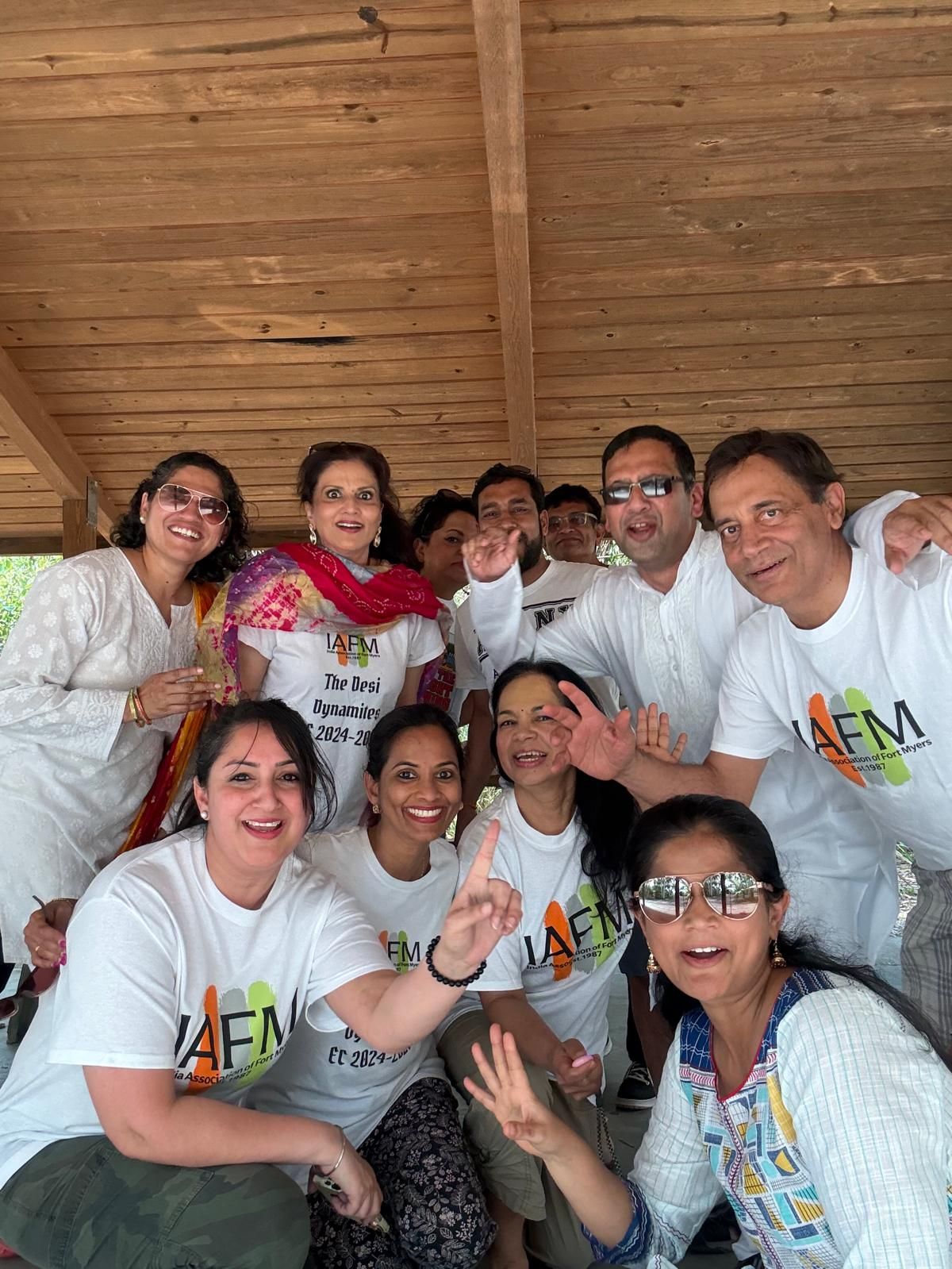 Group of people, mostly wearing white shirts, posing for photo outdoors. Smiling, some giving peace signs.