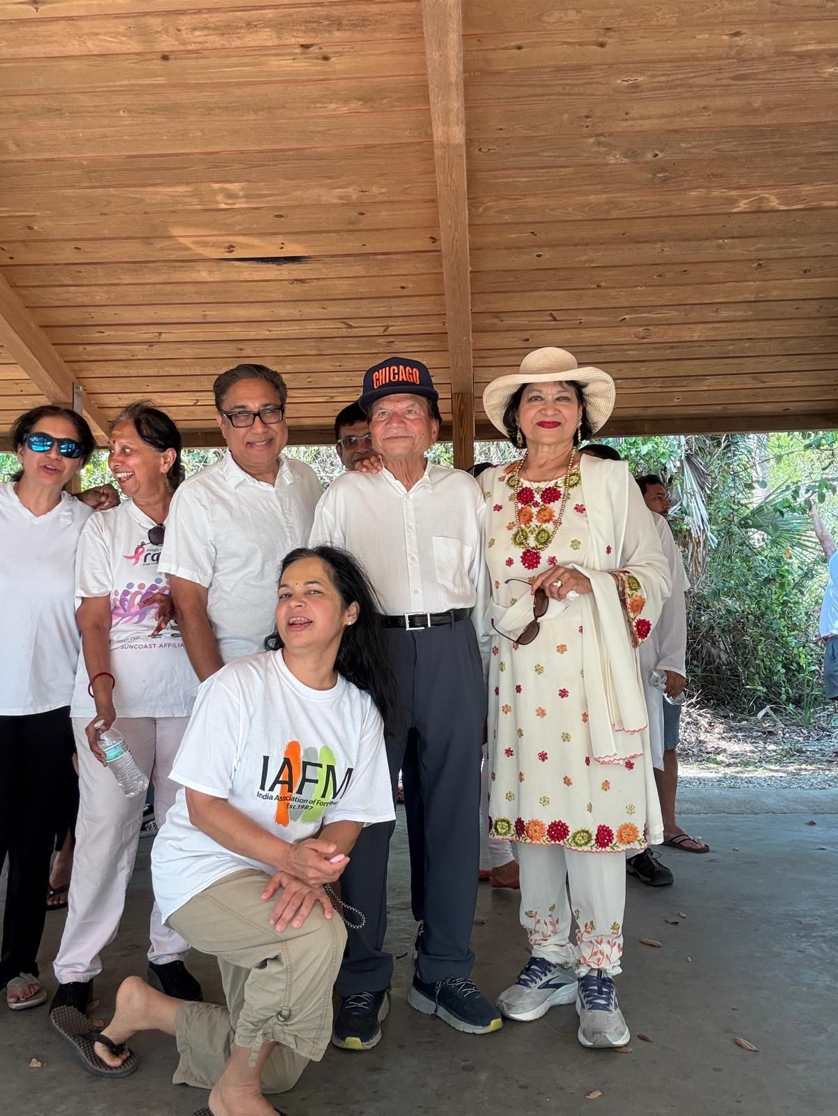 Group of people posing outdoors, some smiling. Wooden shelter overhead.