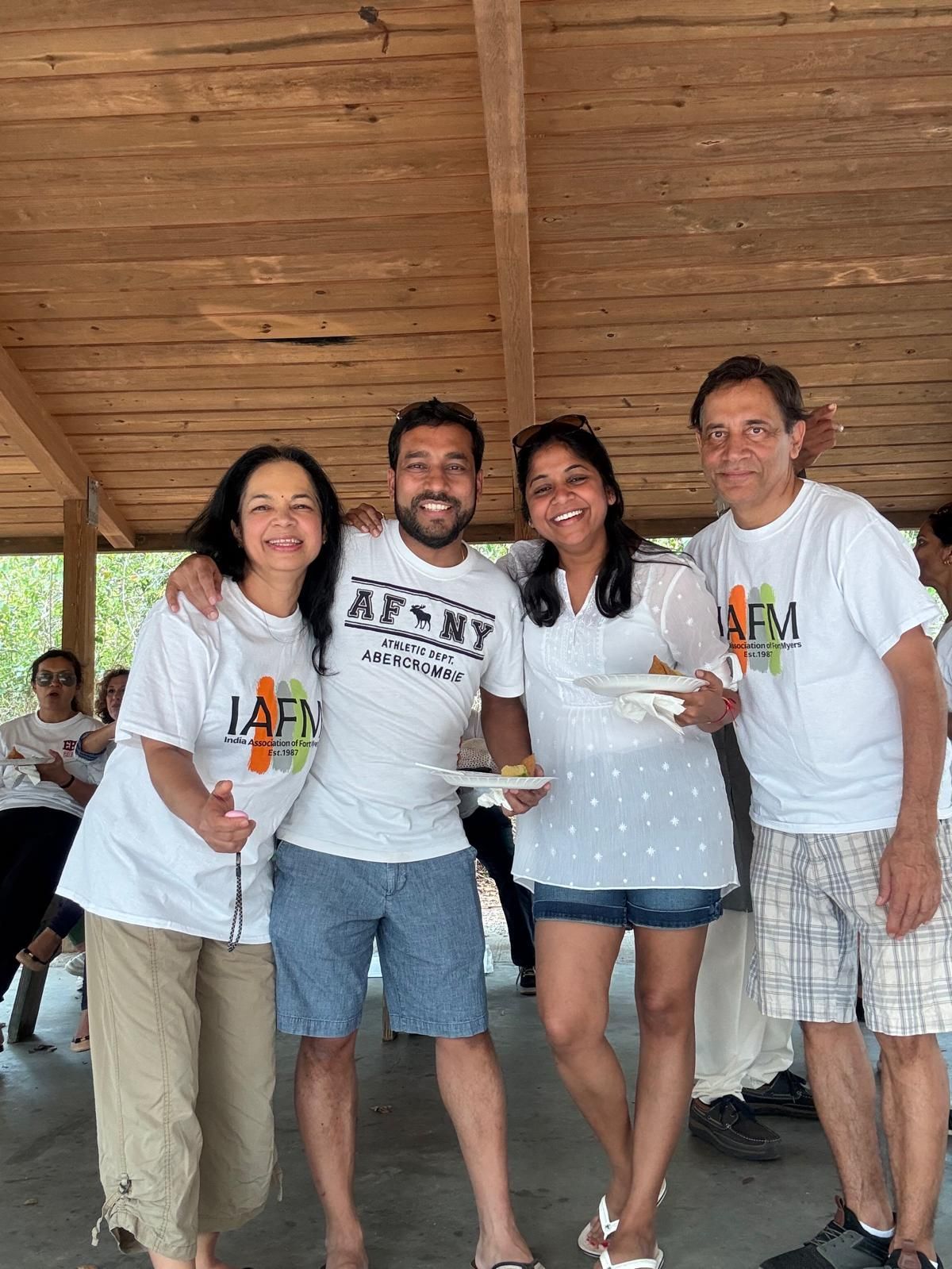 Group of four people at a picnic, smiling and posing for a photo, under a wooden pavilion.