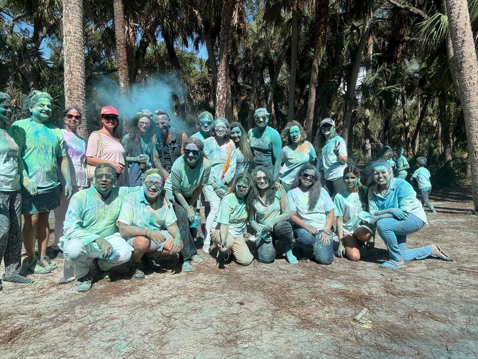 Group of people covered in colorful powder outdoors, posing in front of trees.