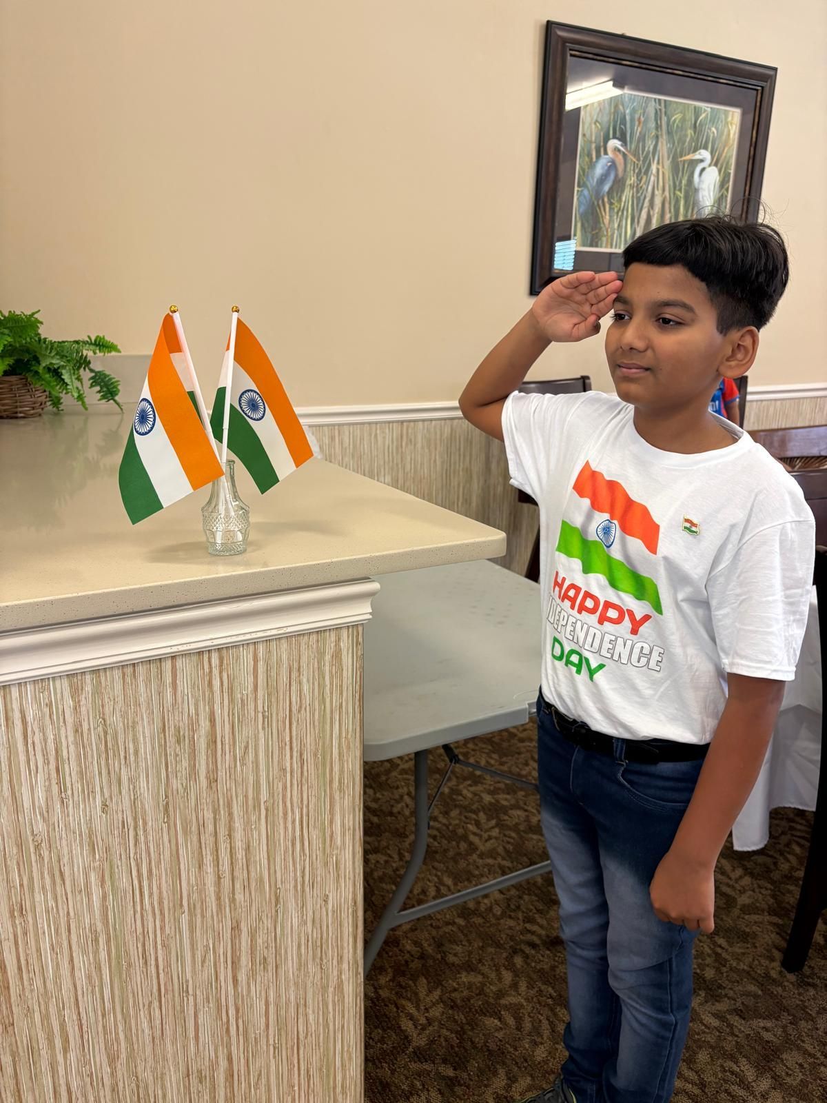 Young boy salutes Indian flag. He wears a t-shirt that says “Happy Republic Day.”