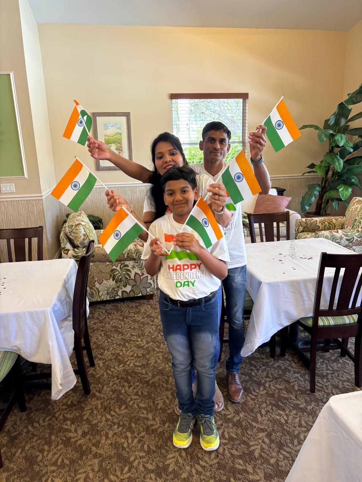 Family holding Indian flags, celebrating; room with tables, festive.