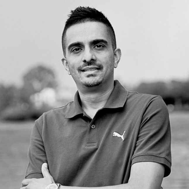 Man with short dark hair wearing a red polo shirt, arms crossed, outdoors near water.